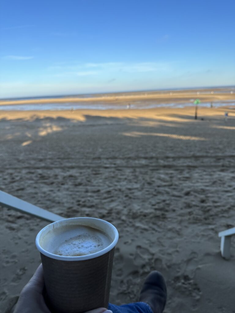 Image shows a beach with the tide out and a coffee cup. 