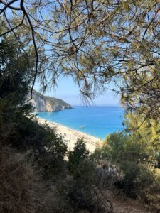 Image shows a beach with blue sea seen from above through greenery. 